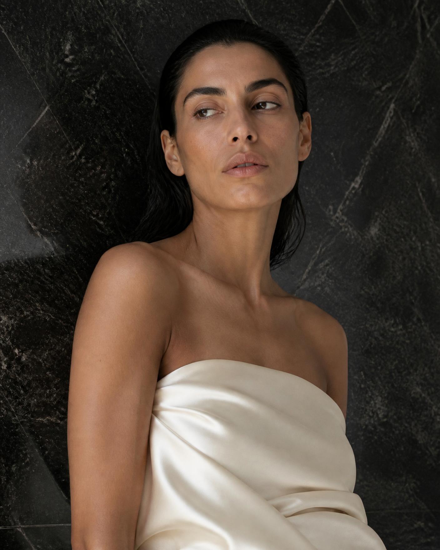 A poised Mediterranean woman in ivory silk against black stone